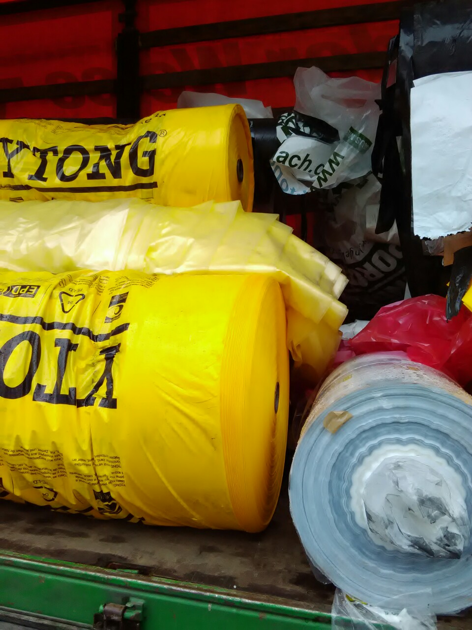 Yellow and white plastic film rolls and loose plastic material loaded in an industrial transport container.