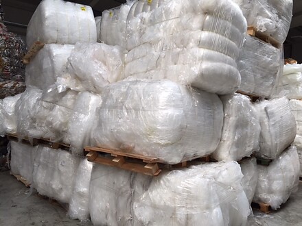 tacked white plastic film bales wrapped in clear stretch film on wooden pallets in a warehouse.