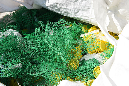 Green plastic netting and yellow plastic components collected in a white bulk bag for recycling.