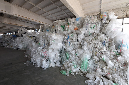 tacked bales of transparent plastic film stored inside an industrial warehouse.