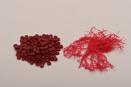 Red plastic pellets and shredded red plastic strands displayed on a white background.