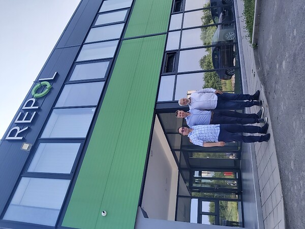 Three people standing in front of the REPOL headquarters building with the REPOL logo above the entrance.